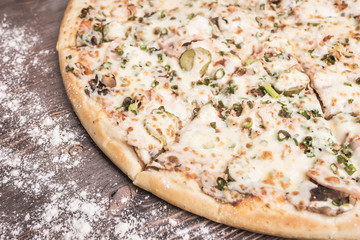 Pizza on the right side of the frame on a brown wooden background sprinkled with flour