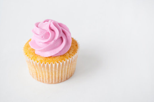 Cupcake with pink whipped cream on white background. The image with copy space. Background for the confectionery menu, cards, greetings, birthday invitations.