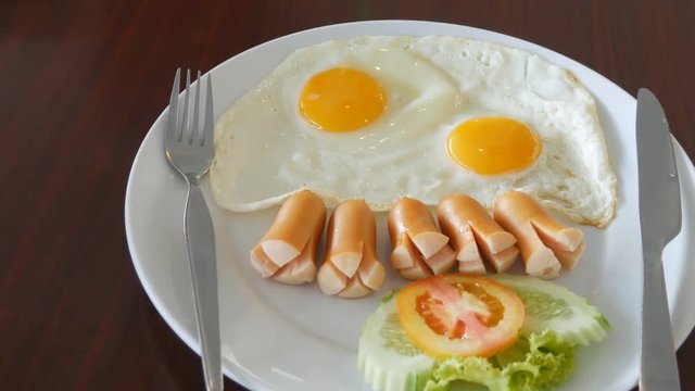 panning shot of fried eggs with sausages, tomatoes on wood table