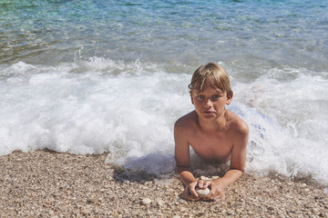 Young child boy having fun in the sea on the waves and enjoying water in summer holiday