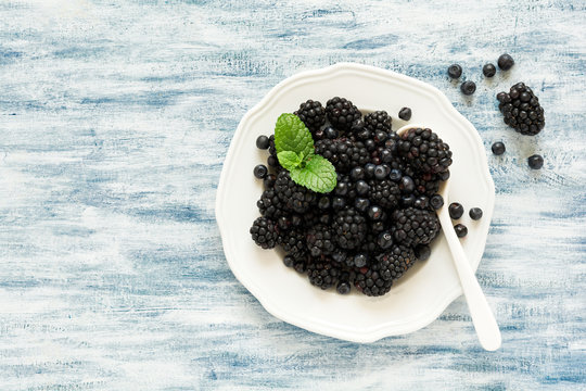 Plate with blackberries and blueberries on blue wooden background. Top view