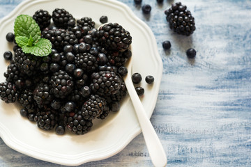 Plate with blackberries and blueberries on blue wooden background. Top view