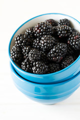 Blue bowl with blackberries on white wooden background