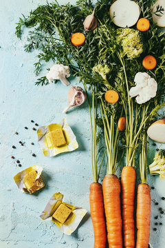 Raw vegetables and bouillon cubes for cooking soup. Young carrot with haulm, broccoli, cauliflower, onion, garlic, salt pepper over turquoise concrete background. Top view. Dinner cooking concept