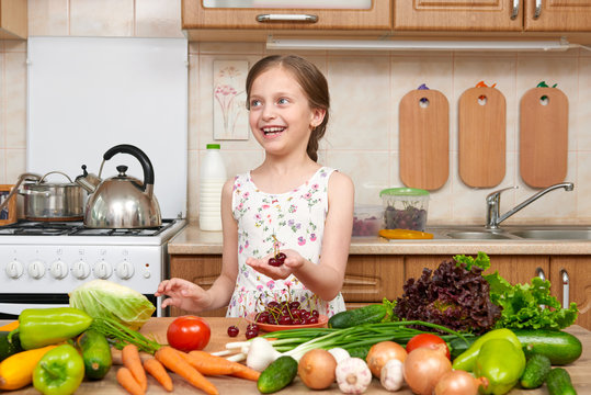 child girl posing with cherry, fruits and vegetables in home kitchen interior, healthy food concept