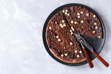Stoff pro Meter Cutting dessert chocolate pizza with dark, milk, white chocolate, served on black plate with mint, knife and fork over gray concrete background. Top view with copy space © Natasha Breen