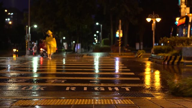 4K Pedestrian man with yellow oilskin jacket struggling to cross street during Typhoon Nesat in Taipei City. Extreme wind and rain in night. Strong hurricane winds with car traffic in road Taiwan.-Dan