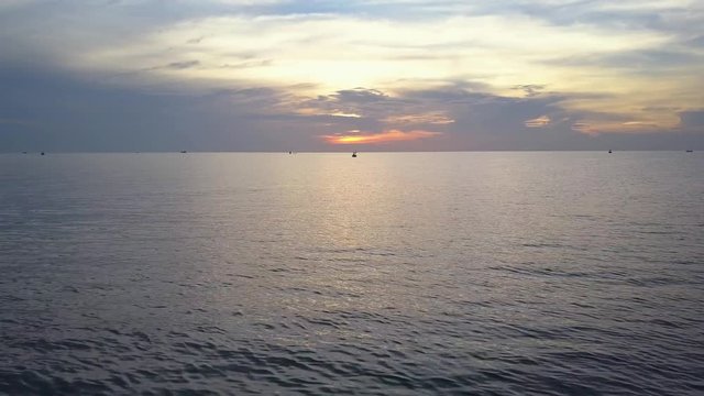 Flying over the sea into the sun and see fishing boat during sunrise by using a drone to take aerial footage
