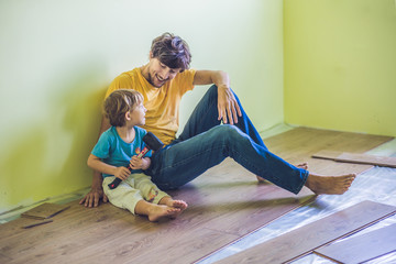 Father and son installing new wooden laminate flooring. infrared floor heating system under...