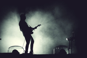 Silhouette of a guitar player in stage lights - obrazy, fototapety, plakaty