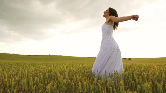 Young emotional woman in the white dress spinning in wheat field.