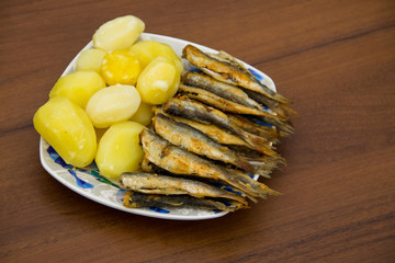Fried baltic herring with boiled potatoes on a plate on wooden background