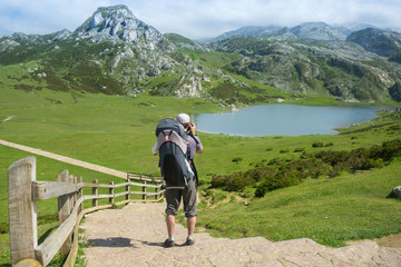 Fototapeta na wymiar Family trip to Spain nature: father with a baby in a backpack hiking on the trail to high mountain lakes in sunny summer day