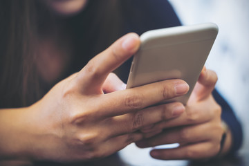 Closeup image of an Asian woman holding , using and looking at smart phone in modern cafe
