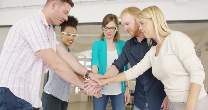 Side view of group of young promising coworkers standing in circle and stacking all together showing high spirit of team unity.