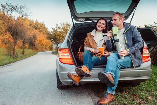 Tea party in car trunk - loving couple drinks hot tea from thermos flask sitting in car trunk