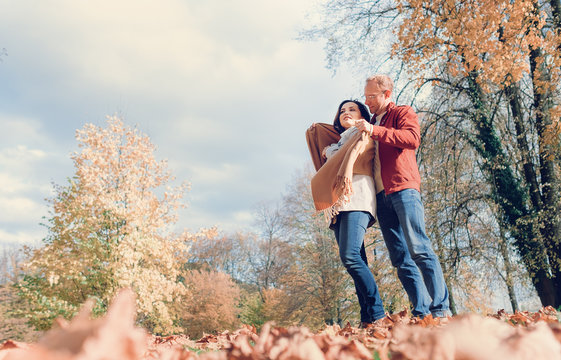 Man covers his wife shoulders with warm shawl in autumn park