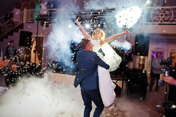 Newly married couple dancing on their wedding party with heavy smoke and multicolored lights on the...
