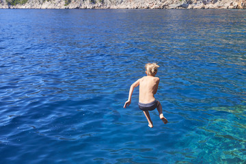 The child boy is jumping into the blue sea