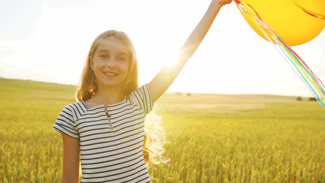 Portrait of happy beatiful girl with balloons smiling on camera on the field background on the sunset time. Close up.