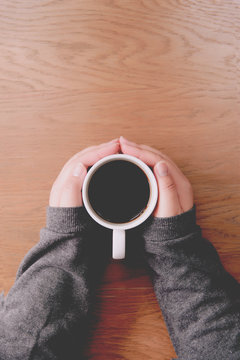 A woman's hand holding a coffee cup on a wooden table top view