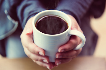 A woman's hand holding a coffee cup on a wooden table top view