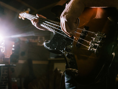 Playing bass guitar strings closeup. Unrecognizable guitarist, music recording studio, dark atmosphere with back light