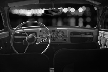 Old cabin, console and steering wheel in a vintage retro car. Night lights. Black and white image.