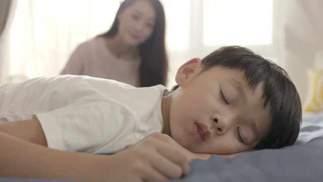 close up of young Asian mother smiling & waking up her son in morning