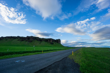 Iceland - Blue sky over street between green meadow and volcanic rocks at dawn