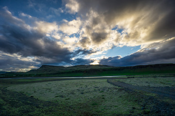 Iceland - Sun breaking through clouds over green volcanic landscape
