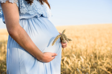 Pregnant woman relaxing in nature on a beautiful sunny day. A crop of a pregnant woman's stomach with field in the background.