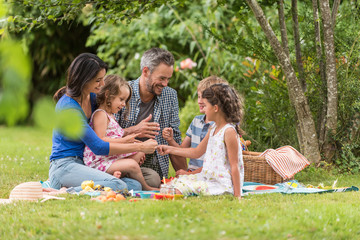 Cheerful family sitting on the grass during un picnic in a park - obrazy, fototapety, plakaty