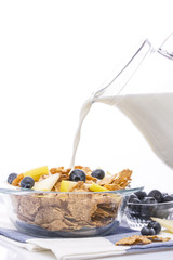 Muesli with apples and blueberries on white background. Milk is pouring from the jug.