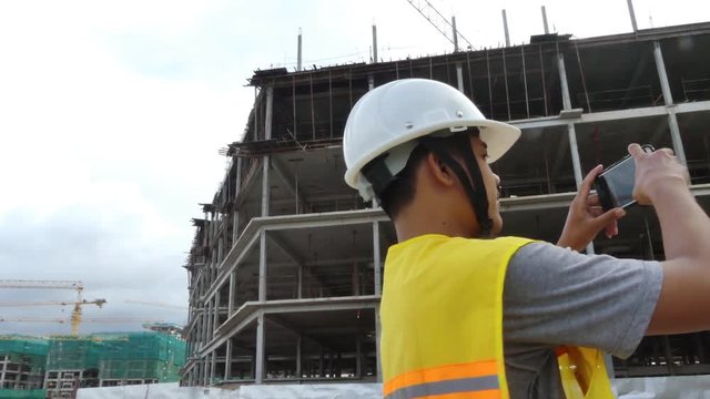 Multicultural ethnic project manager/construction worker/architect/tradesman makes a smartphone video documentary of his site at a building project; 2nd site with cranes can be seen