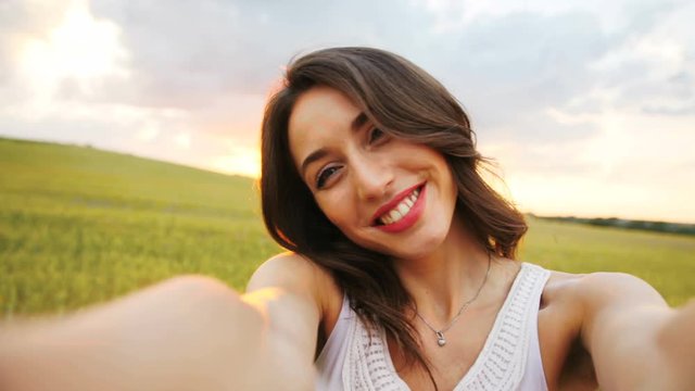 Young attractive woman making selfie on camera, possing and smiling on golden wheat field background.