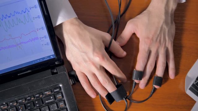 Top view on veiny trembling hands attached to a polygraph. 