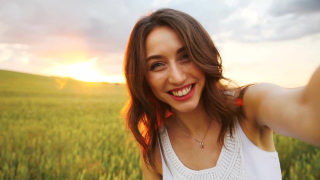Happy caucasian woman making selfie on camera, possing and smiling on golden wheat field background.