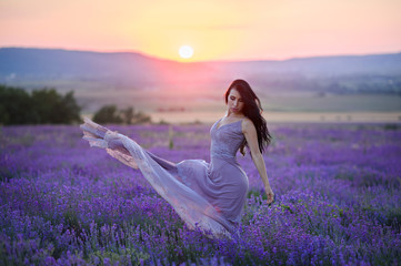 Fototapeta na wymiar Beautiful woman in a field of lavender on sunset. Woman in amazing dress walk on the lavender field.