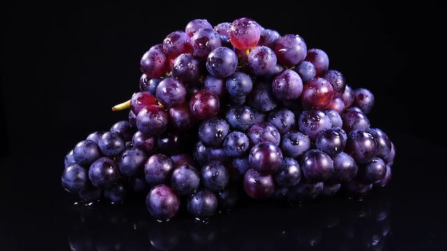 Bunches of red grapes with drops of water rotates on black mirror background in 4K. Closeup view shot.
