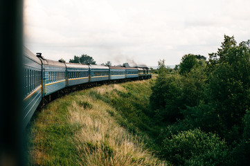 Photo of riding train among summer nature.  View out of window. Travelling by train.  Railroad turn. Going to vacation. Tourism and voyage.  Railway outdoor.  Vintage locomotive moving with old wagons