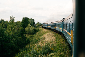 Photo of riding train among summer nature.  View out of window. Travelling by train.  Railroad turn. Going to vacation. Tourism and voyage.  Railway outdoor.  Vintage locomotive moving with old wagons