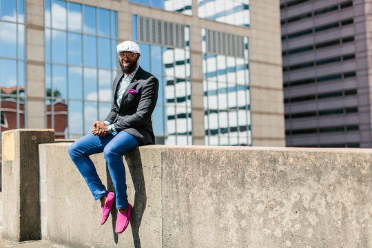 A handsome young male wearing stylish attire sitting outdoors in the city