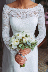 Beautiful wedding bouquet with white roses and peonies. In a bride hands in narrow, elegant white dress