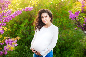 Beautiful pregnant woman hugging her belly in the park at sunset