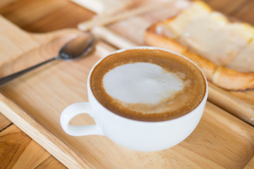 Hot drink coffee with white foam in the white cup. wooden tray and table with bread slice toast
