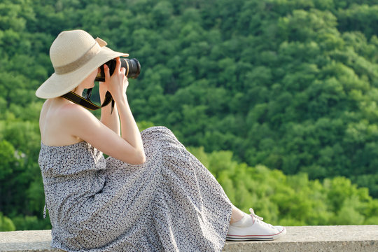 Girl in hat takes pictures against the background of green forest