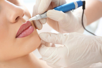 Young woman having permanent makeup on lips in beautician salon - obrazy, fototapety, plakaty