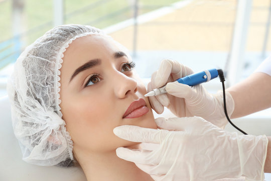 Naklejki Young woman having permanent makeup on lips in beautician salon