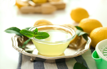 Glass bowl with lemon juice in metal tray on white background